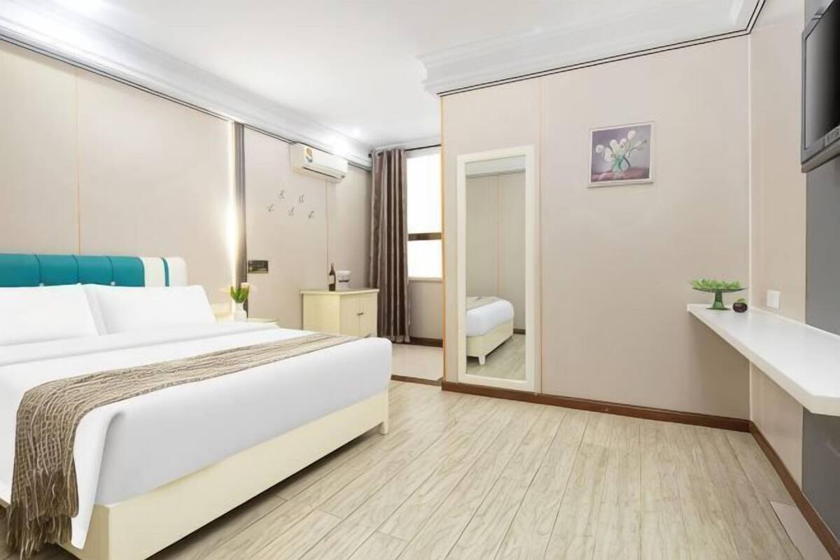 A hotel room with a bed, bedside table, mirror, and a small desk with a chair.