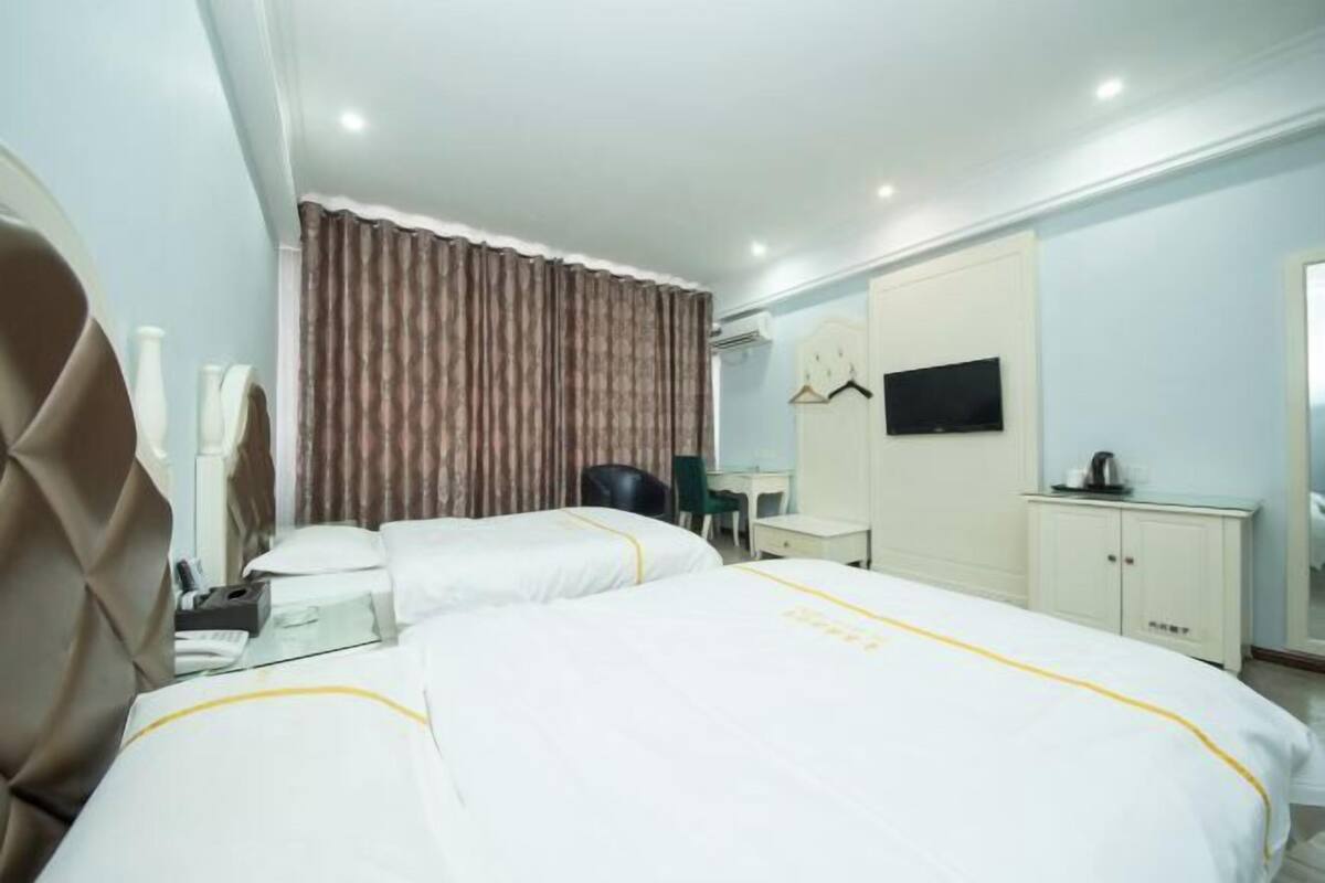 A hotel room with two beds, a desk, a chair, a television, and a wardrobe.