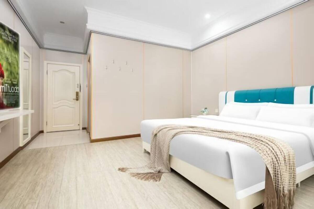 A bedroom with a bed, a nightstand, a door, and a wall-mounted shelf.