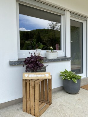 A wooden sign with "Willkommen" and hearts, a potted plant, and a window with a view of trees and a house. - Quiet living in an idyllic location on the beautiful High Rhine - in the Black Forest (Waldshut-Tiengen)