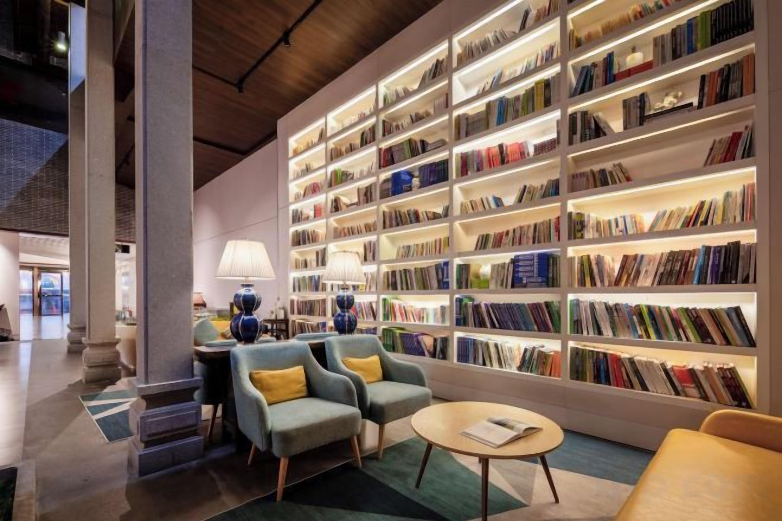 A modern library with bookshelves, seating, and a lamp.
