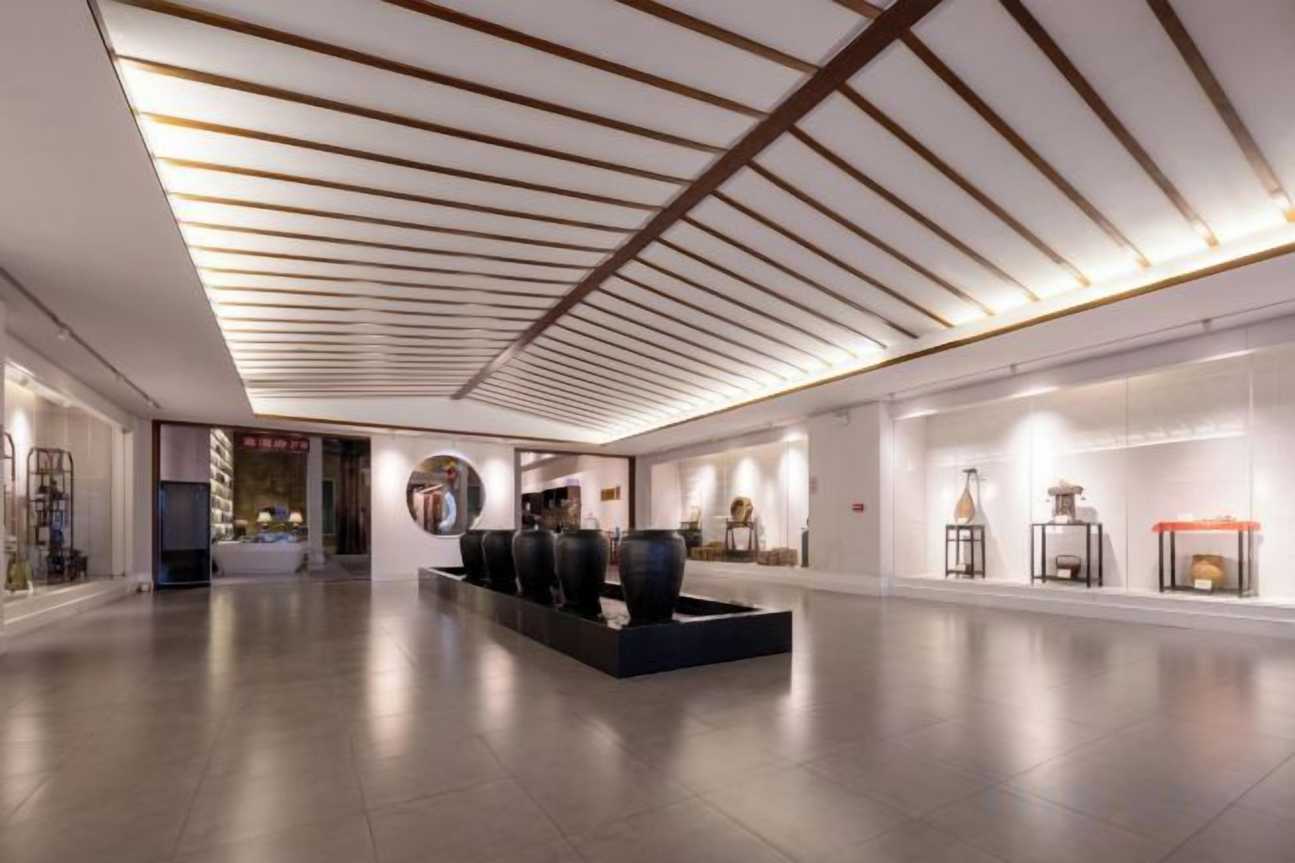 Un vestíbulo espacioso con un diseño moderno de techo, una recepción y una exhibición de objetos decorativos.