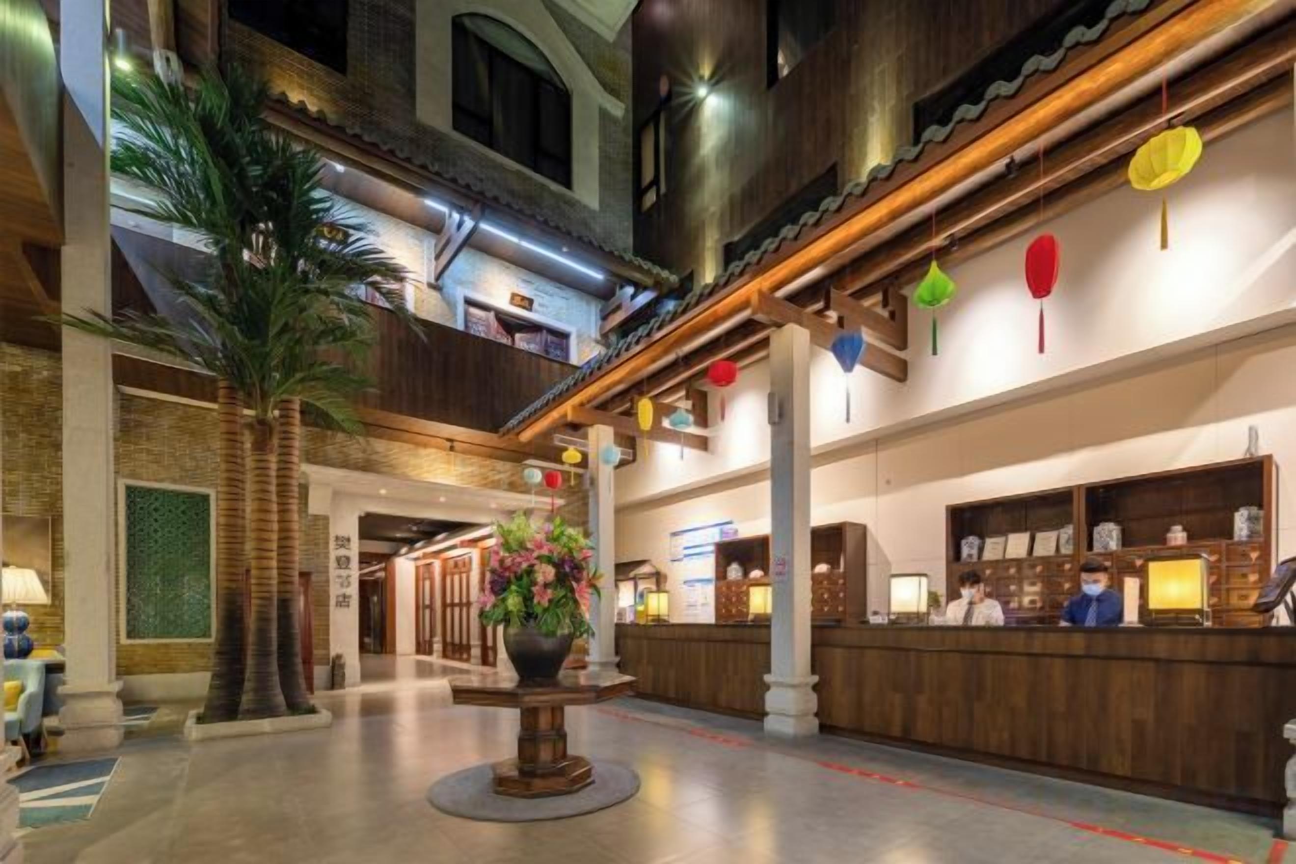 Un hall d’hôtel avec un comptoir d’accueil, une grande plante en pot et un escalier menant à un étage supérieur.