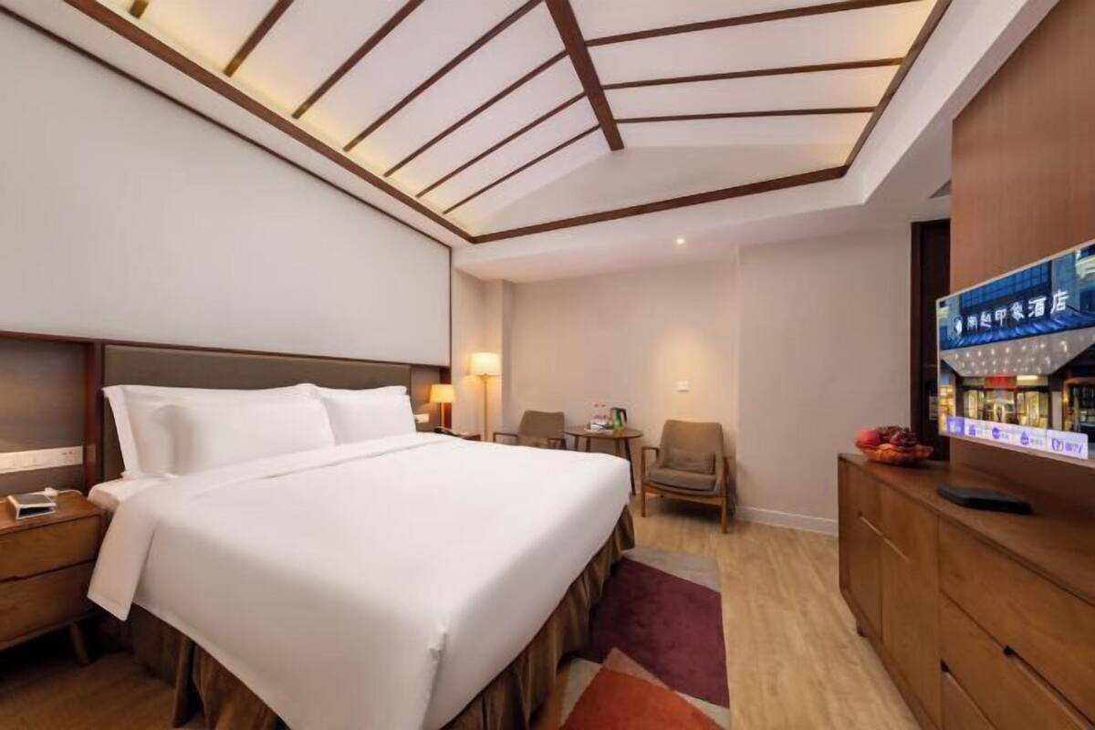 Ein Hotelzimmer mit Bett, Nachttischen, Schreibtisch, Stühlen, Fernseher und einer Decke mit Holzbalken.