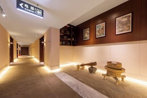 A hotel corridor with a directional sign, wooden wall decor, and a bench.