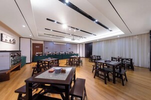 A spacious dining area with multiple tables and chairs, a counter with food display, and a kitchen area in the background.