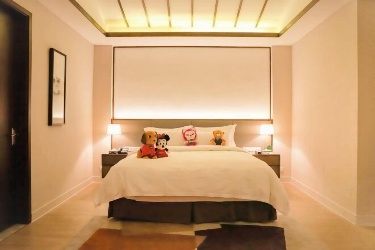 Une chambre d’hôtel avec un grand lit, des lampes de chevet, un tableau encadré au mur et une porte sur le côté gauche.
