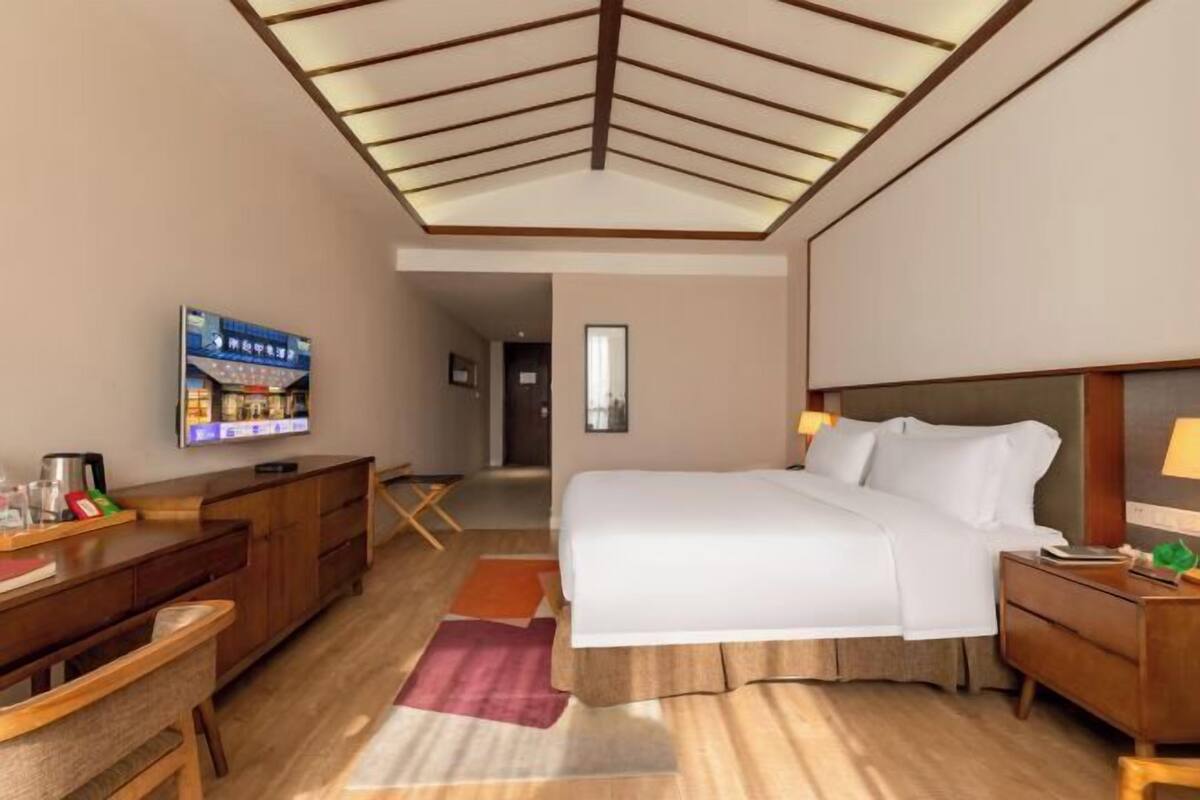 Ein Hotelzimmer mit Bett, Schreibtisch, Stuhl, Fernseher und Blick auf den Flur.