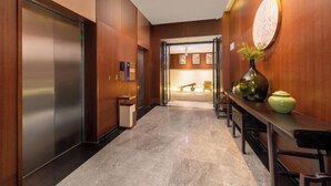 Un vestíbulo de hotel moderno con suelo de mármol, paredes de madera, una recepción y un ascensor.
