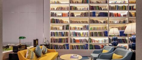 A modern library with bookshelves, a yellow sofa, and two armchairs.