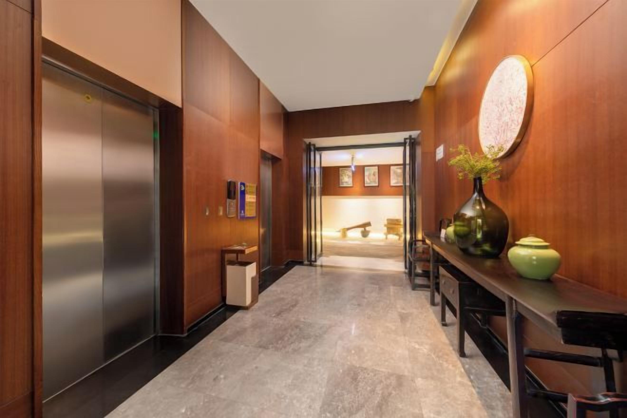 A hallway with a marble floor, wooden walls, a reception desk, and a door leading to a room.
