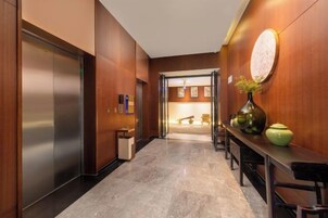 A hallway with a marble floor, wooden walls, a reception desk, and a door leading to a room.