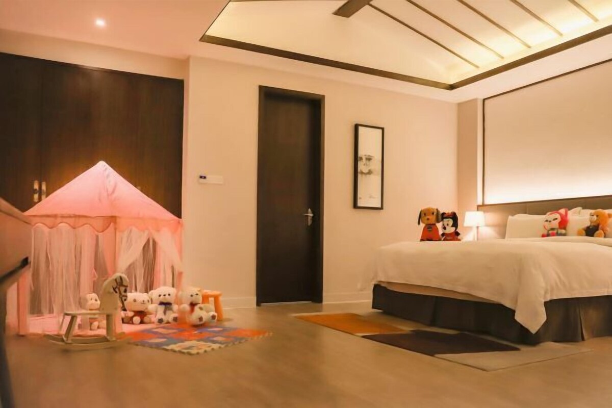Een slaapkamer met een bed, een deur, een kleintje tafel met speelgoed en een tentachtige constructie.