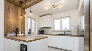 A modern kitchen with white cabinets, a wooden countertop, and a built-in dishwasher. There are hanging lights and a window providing natural light.