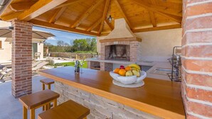 An outdoor kitchen area with a brick oven, a wooden table with a fruit bowl, and a brick column.