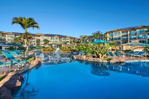 Ein Poolbereich eines Resorts mit mehreren Liegestühlen, einer Palme und einem Gebäude mit Balkonen.