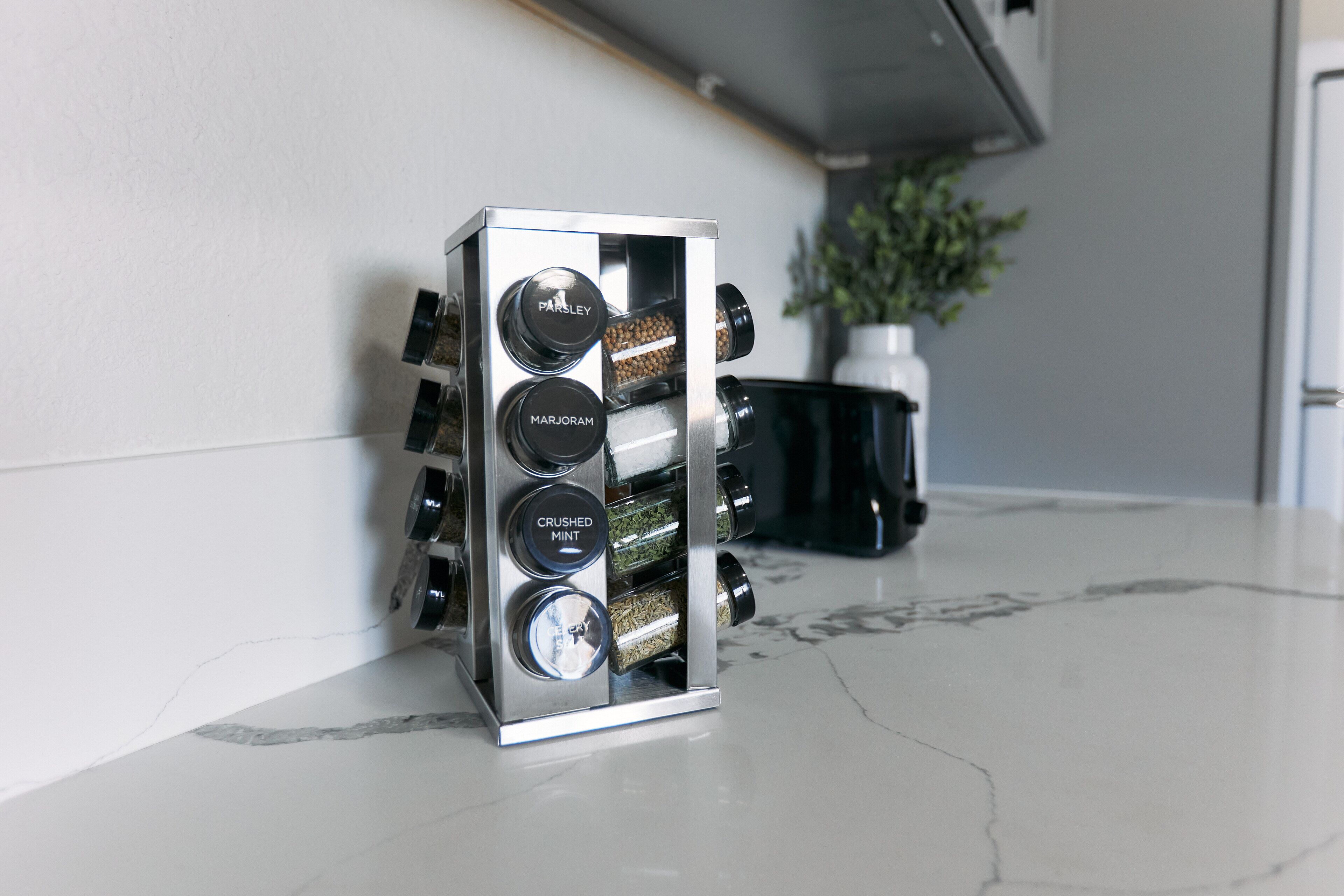 A stainless steel spice rack with labeled compartments for parsley, marjoram, crushed mint, and celery seed.