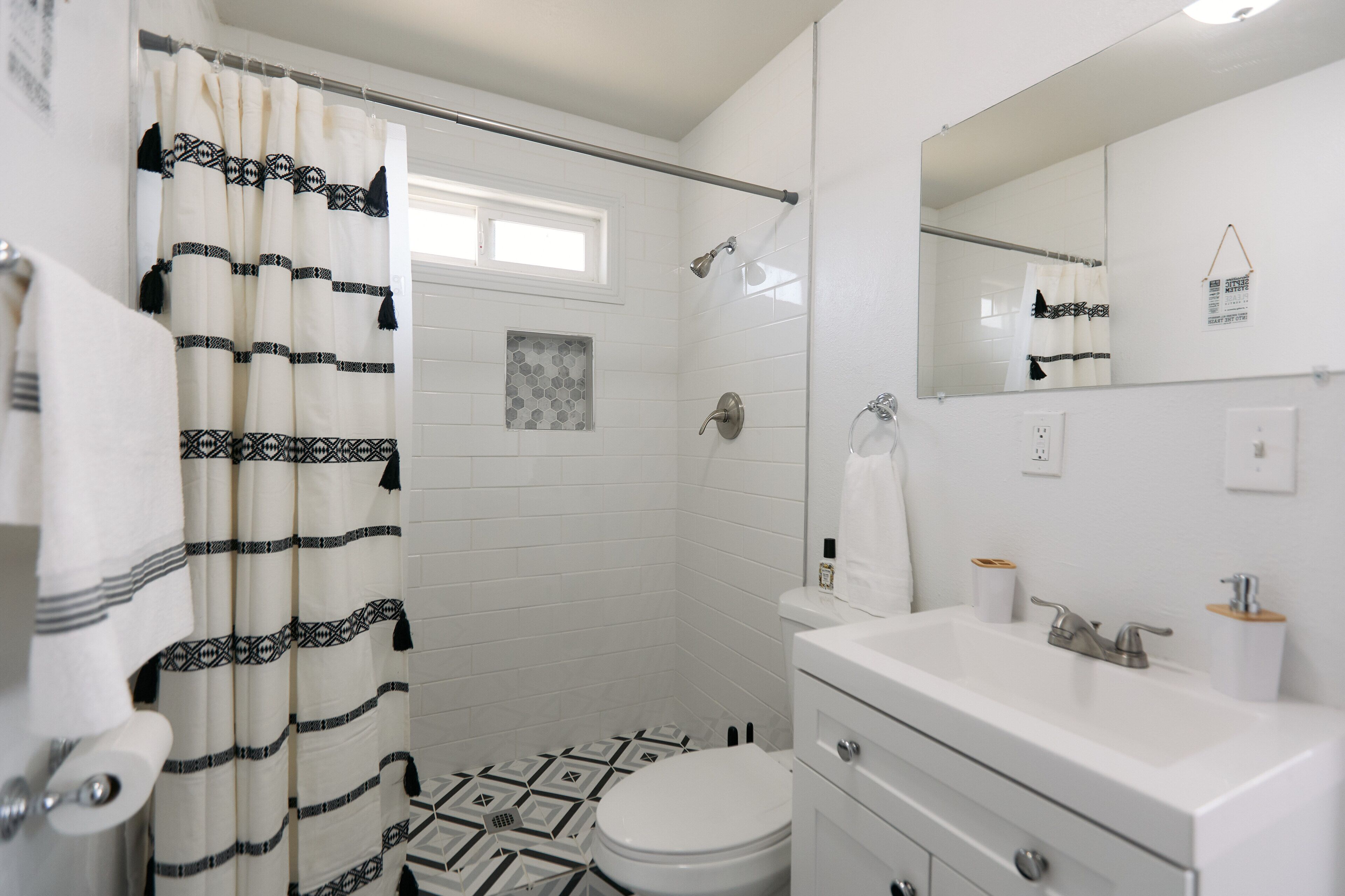 Un baño con inodoro blanco, lavamanos con espejo y zona de ducha con cortina.