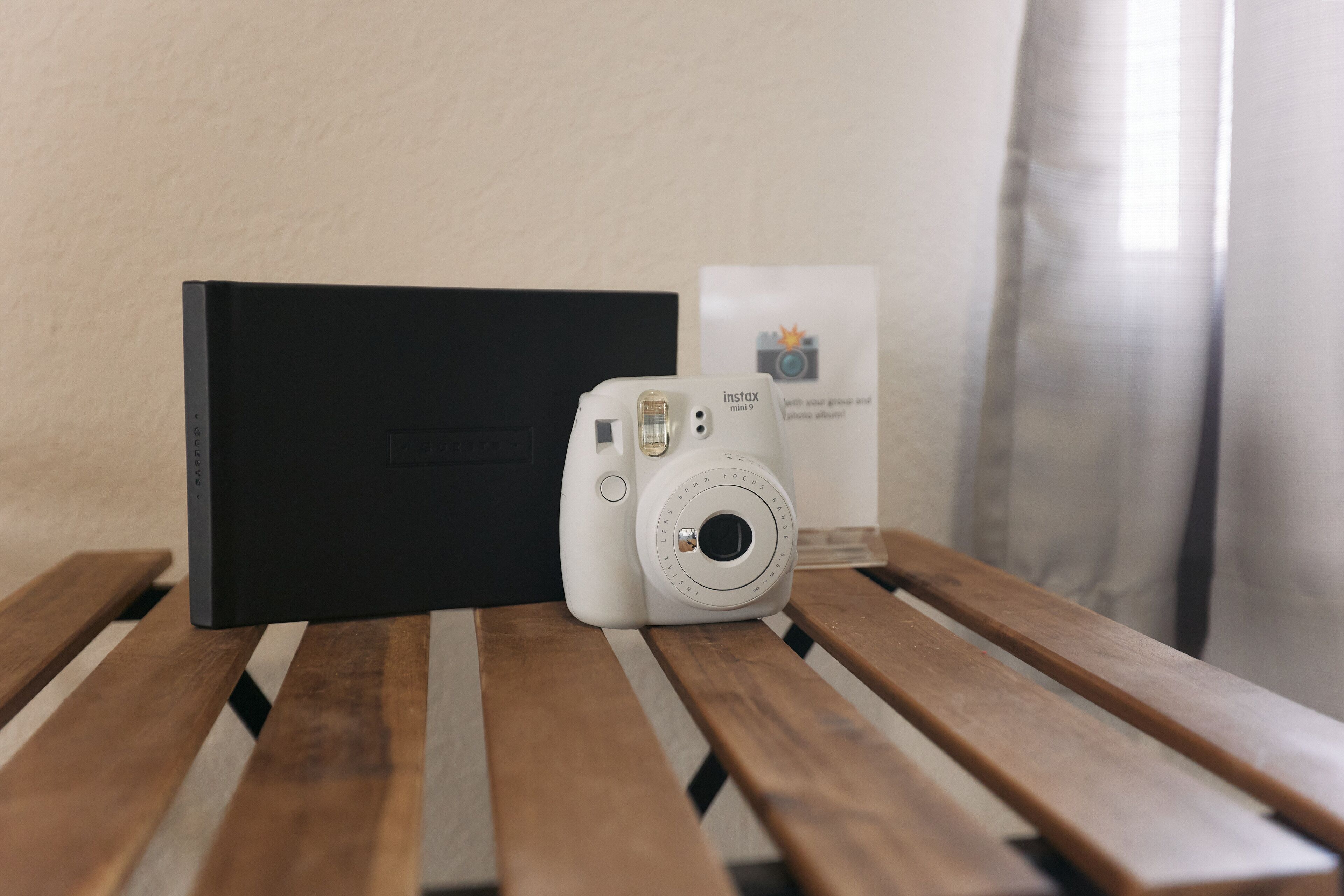 A white camera on a wooden bench with a black box and a sign in the background.