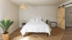 Um quarto com uma cama, uma luminária pendente, decoração na parede, uma planta e uma porta deslizante.
