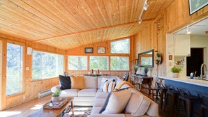 A cozy cabin with a wooden interior, a large sofa, a dining area, and a kitchen with bar stools. - Gated Carmel Valley Retreat with 20 Acres, Pool & Hot Tub (Carmel Valley)