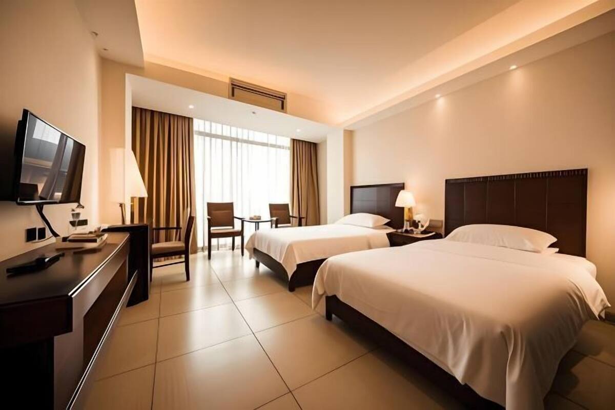 Ein Hotelzimmer mit zwei Betten, einem Schreibtisch mit Fernseher, einem Sessel und einem kleinen Tisch.