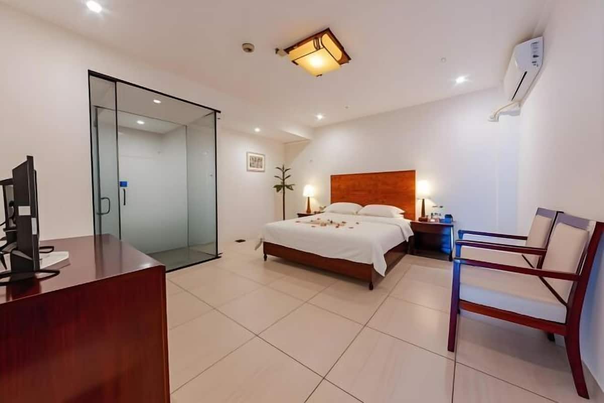 Ein Hotelzimmer mit Bett, Schreibtisch, Stuhl, Nachttisch und Wandklimaanlage.