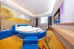 Ein modernes Hotelzimmer mit einem runden Bett, einem großen Gemälde an der Wand, einem Flachbildfernseher und Holzboden.