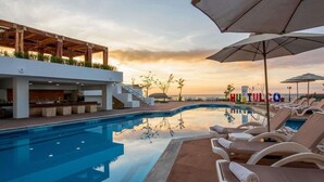 A poolside area with lounge chairs, a bar, and a view of the sunset. - Royal Club at Park Royal Beach Huatulco - Vacation Club (Santa María Huatulco)