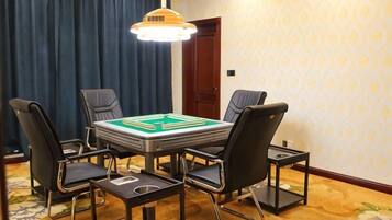 A hotel room with a dining table, four chairs, a chandelier, and a patterned carpet.