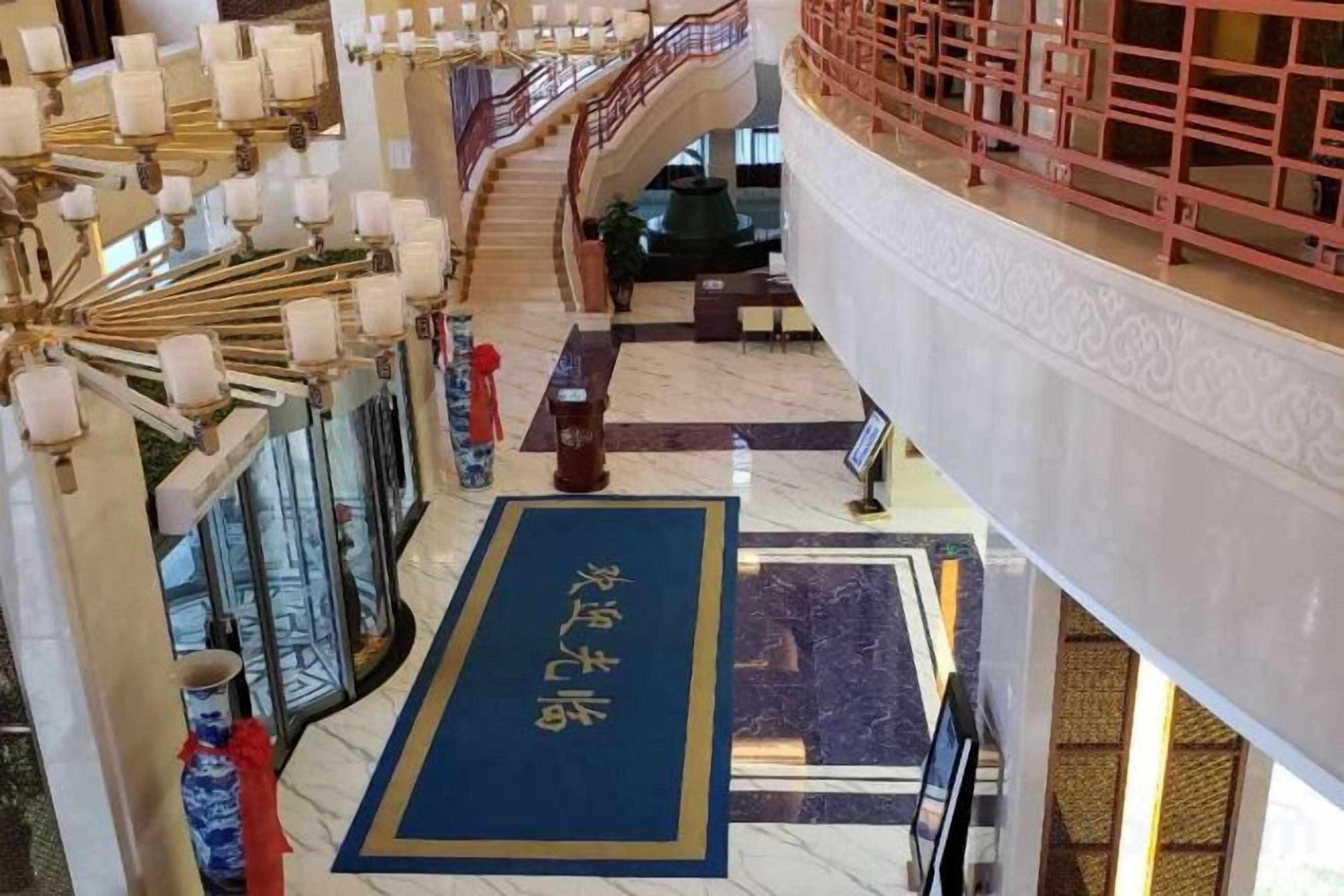 A hotel lobby with a blue carpet, a staircase, and traditional decor.