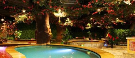 An indoor swimming pool with a curved edge, surrounded by artificial trees and flowers.