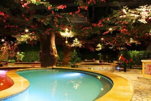 An indoor swimming pool with a curved edge, surrounded by artificial trees and flowers.