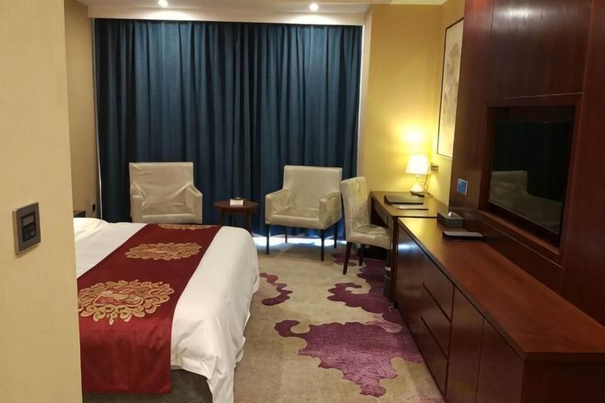 Une chambre d’hôtel comprenant un lit, deux fauteuils, un bureau, une télévision et une grande fenêtre avec des rideaux.