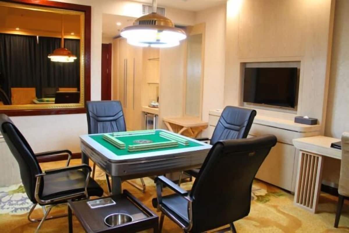 Une pièce avec une table recouverte de feutre vert, quatre chaises noires, un grand miroir, un téléviseur et un luminaire au plafond.