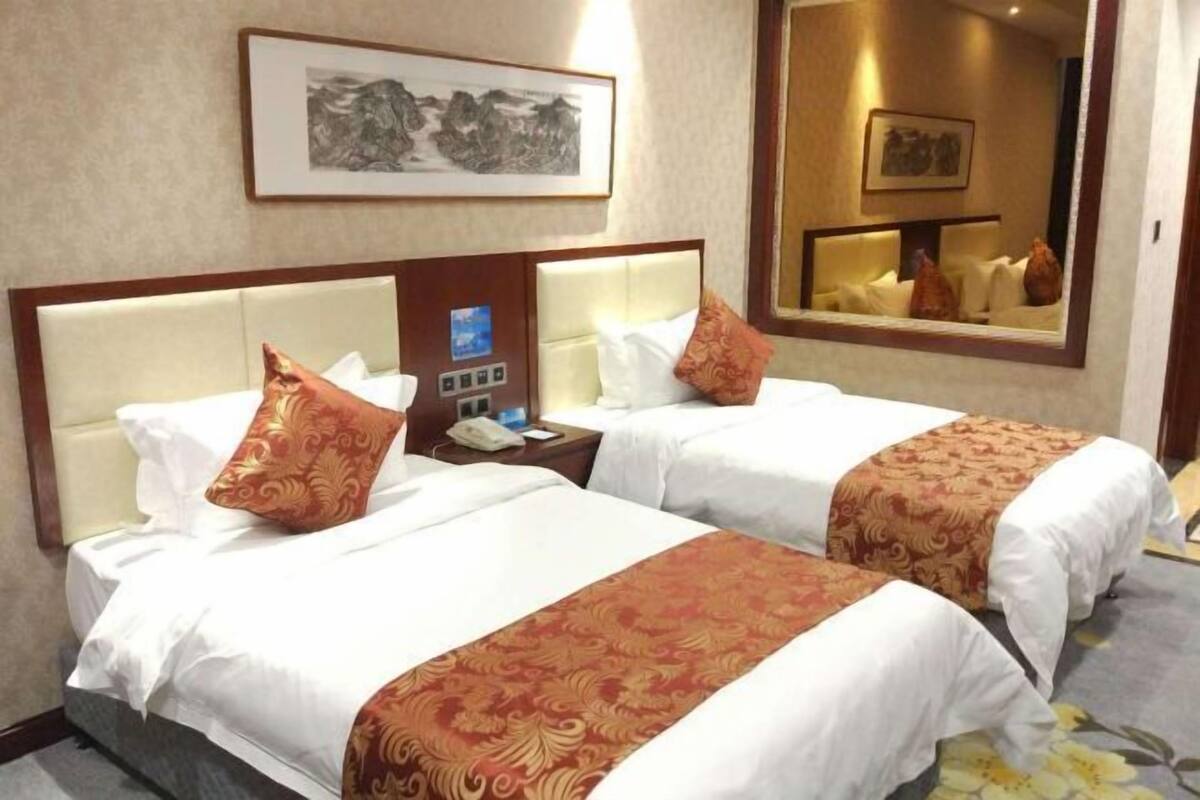Une chambre d’hôtel avec deux lits, une table de chevet avec un téléphone et un miroir qui reflète la pièce.