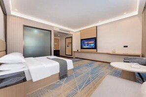 A hotel room with a bed, a TV, a seating area, and a carpeted floor. - Boying Business Hotel (Jiangmen)
