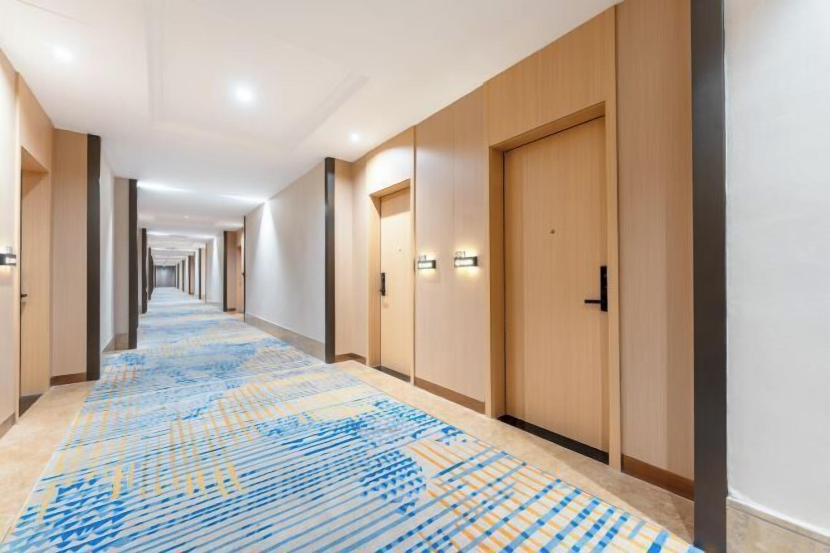 A hotel corridor with wooden doors, a patterned carpet, and recessed lighting.