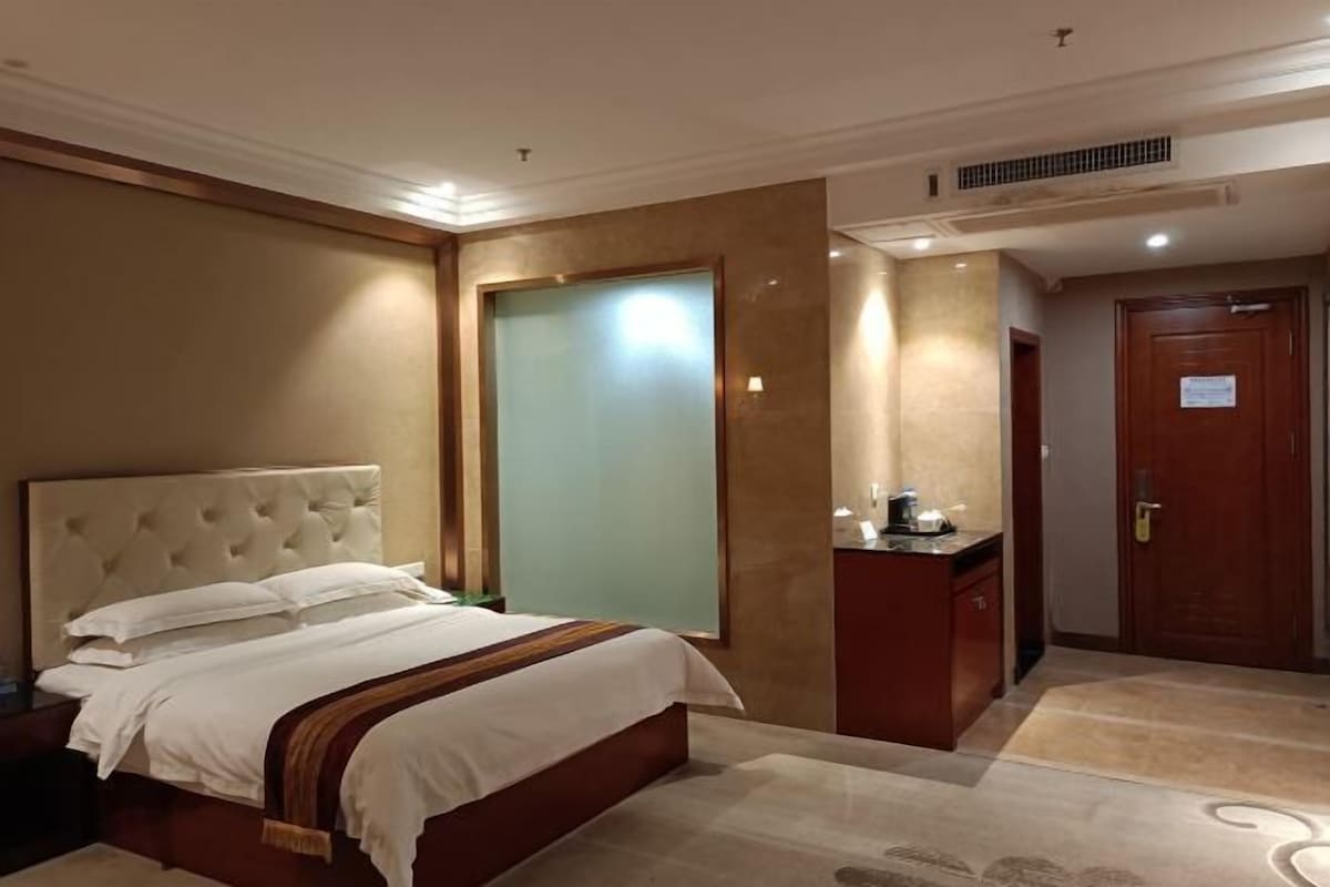 A hotel room with a large bed, a small desk, a mirror, and a door.