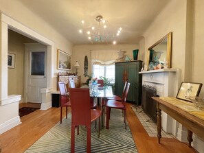 A dining area with a chandelier, wooden dining table, red chairs, and a patterned rug.