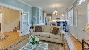 A spacious living room with a beige sofa, a coffee table with a vase of flowers, and a staircase leading to another level. - Historic 4-Bedroom Manor | Walk to Music Row & Vanderbilt | Family Retreat (Nashville)