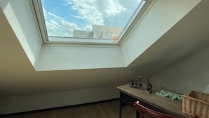 Ein Zimmer mit Oberlichter, einem kleinen Tisch, einem Fahrrad, einem Stuhl und einem Korbwägelchen.