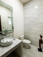 A modern bathroom with a large mirror, a round sink, and a toilet.