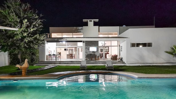 A modern house with a swimming pool, a dining area, and a well-lit exterior at night.