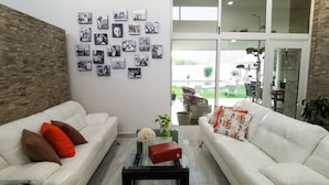A living room with two white sofas, a glass coffee table, and a wall decorated with black-and-white photos.