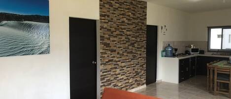 Een moderne woonkamer met een bank, een keukenhoek met een magnetron en een waterdispenser, en een gestructureerde muur.