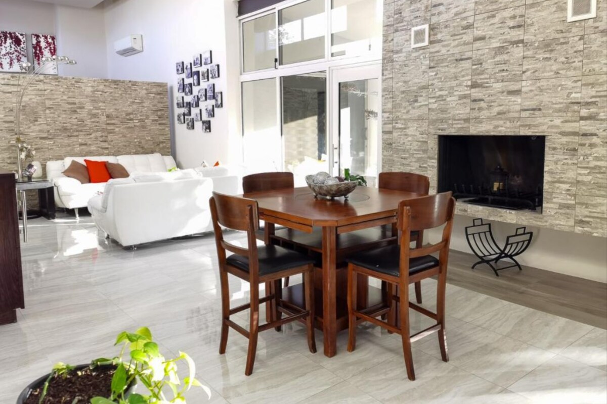 A modern living room with a dining area, a fireplace, and a large window.