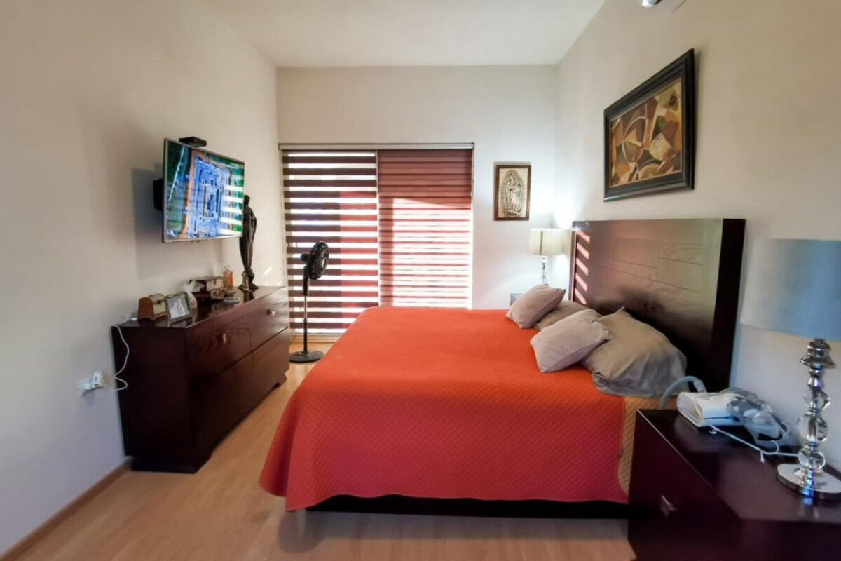Ein Schlafzimmer mit Bett, Kommode, Nachttisch, Lampe und Bildern an den Wänden.