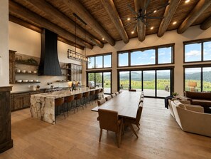 A spacious kitchen with a large island, bar seating, and a view of a mountainous landscape through large windows.