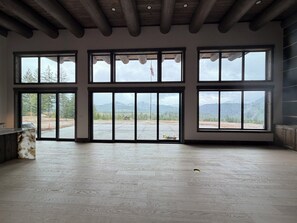 A spacious room with large windows, wooden floors, and a view of mountains.